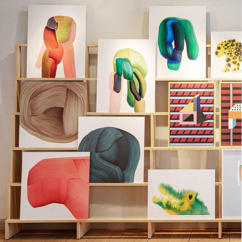 Wooden shelf with various abstract artworks on a neutral wall.